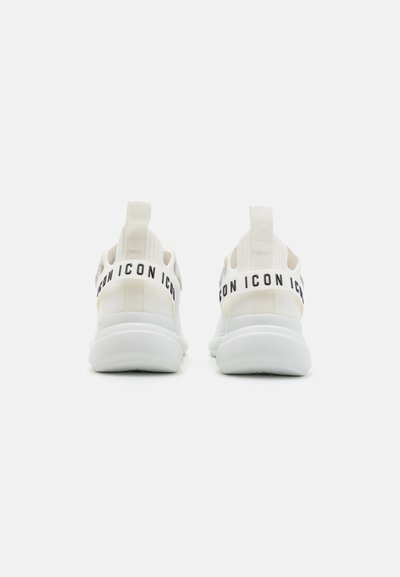 Hvide atletiske sneakers med en tekstureret stofoverdel, sort branding på bagre strop og en afrundet, polstret sål.