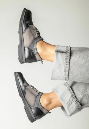 Zapatos negros y grises con cordones que presentan una combinación de cuero y gamuza, con un acabado texturizado y una suela de goma flexible.