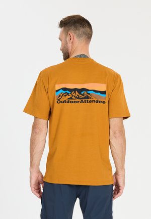 Mann, von hinten gesehen, trägt ein senffarbenes T-Shirt mit Berggrafik und dem Text "Outdoor Attendee", kombiniert mit dunkelblauen Hosen.