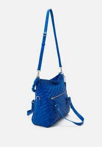 Gepolsterte blaue Handtasche mit verstellbarem Trageriemen, ausgestattet mit einer Reißverschlusstasche auf der Vorderseite und strukturierter Oberfläche. Akzente sind silberne Hardware.