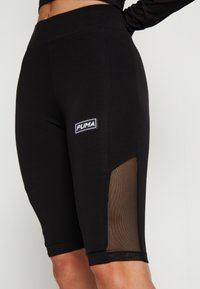 Zbliżenie osoby w czarnych legginsach Puma z wysokim stanem i siateczkową wstawką na zewnętrznej stronie uda.