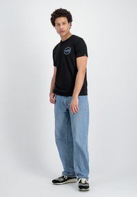 T-shirt en coton noir avec un logo NASA coloré à l'avant, associé à un jean décontracté bleu clair et des baskets noires.