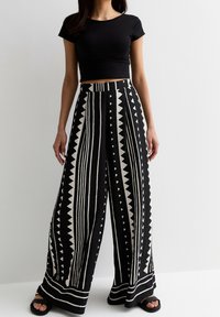 Zwart-witte wijde broek met verticale strepen en driehoekige vormen, gemaakt van een lichtgewicht materiaal, gecombineerd met een zwart cropped topje.
