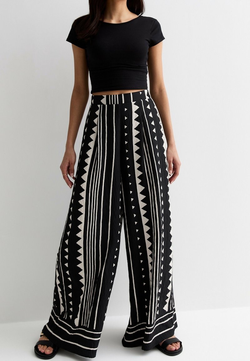 Zwart-witte wijde broek met verticale strepen en driehoekige vormen, gemaakt van een lichtgewicht materiaal, gecombineerd met een zwart cropped topje.