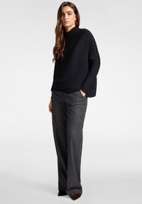 Top negro de canalé con diseño de cuello alto, combinado con pantalones de rayas grises. Los pantalones tienen un corte holgado y un sutil brillo.