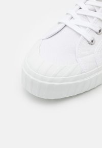 Białe sneakersy z teksturowaną siateczkową cholewką, gumowym noskiem z pionowymi rowkami i płaskimi sznurowadłami. Minimalistyczny design o czystej estetyce.