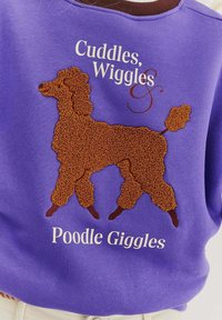 Fialová mikina s vyšitým designem hnědého pudla a textem "Cuddles, Wiggles & Poodle Giggles" v bílém písmu.