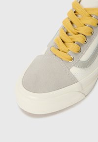 Gray suede and cream canvas sneaker with yellow laces, featuring a smooth white rubber sole and side accents in light blue.