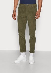 Olive green corduroy pants with a slim fit, featuring a button closure, front pockets, and rolled cuffs, paired with white sneakers.