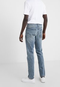 Vaqueros de mezclilla azul claro con corte recto, que presentan un diseño clásico de cinco bolsillos y un desgastado sutil, combinados con una camiseta blanca lisa.