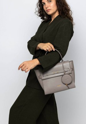 Gray structured handbag with smooth texture, gold hardware accents, and a detachable round charm. Woman wearing an olive green outfit.