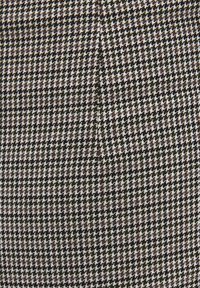 Tæt vævet stof med et klassisk sort, hvidt og brunt houndstooth-mønster, der danner små, gentagne, takkede former.