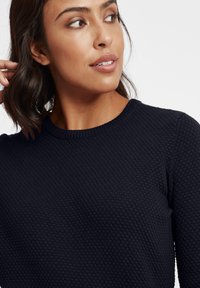 Marineblaues Strickpullover mit einem strukturierten, Wabenmuster und einem gerippten Rundhalsausschnitt. Nahaufnahme, die sich auf den Ausschnitt und den Schulterbereich konzentriert.