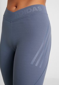 Wysokie niebieskie legginsy sportowe wykonane z elastycznej tkaniny, charakteryzujące się gładką teksturą i trzema subtelnymi paskami po boku.