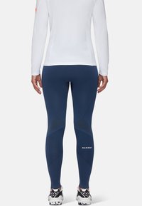 Leggings blu navy con dettagli testurizzati, caratterizzati da un design aderente e logo sulla parte bassa della gamba, abbinati a una camicia lunga bianca.