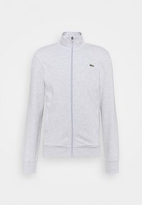 Ljust grå zip-up sweatshirt med hög krage, långa ärmar, ribbade mudd och nederkant, med en liten grön broderad logotyp på bröstet.