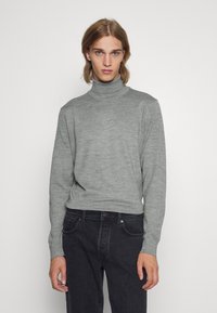 Grå turtleneck genser med lange ermer, laget av mykt strikket stoff. Brukt sammen med mørke jeans. Enkel, figurnær design med ribbestrikket krage.