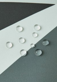 Przezroczyste krople na teksturowanej tkaninie z geometrycznymi kształtami w odcieniach szarości i bieli, o różnej wielkości i szczegółach odbijających światło.