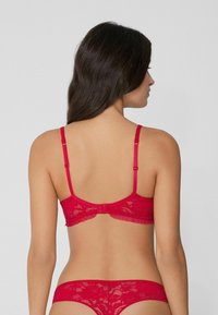 Červený krajkový komplet spodního prádla obsahující balkónovou podprsenku s nastavitelými ramínky a odpovídající tanga, zdobené volánkovým lemem.