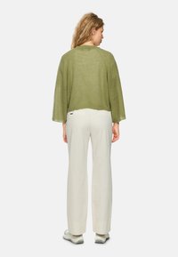 Olivgrüner, kürzer geschnittener Strickpullover mit weiten Ärmeln, kombiniert mit lockeren weißen Hosen. Weiche Textur, lässiges Design und minimale Hardware-Details.