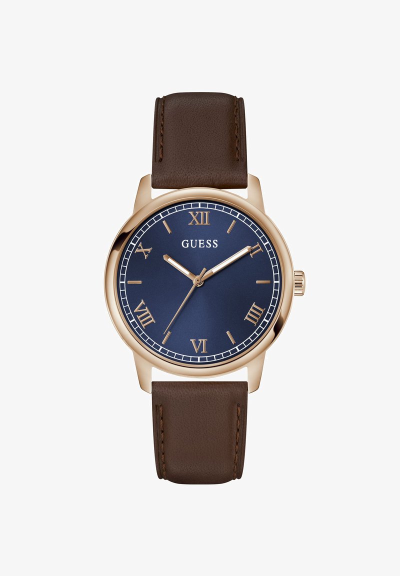 Ρολόι χειρός με κάσα από ροζ χρυσό, σκουρομπλε καντράν, χρυσούς λατινικούς αριθμούς, καφέ δερμάτινο λουράκι και το λευκό όνομα της μάρκας «GUESS» στο κέντρο.