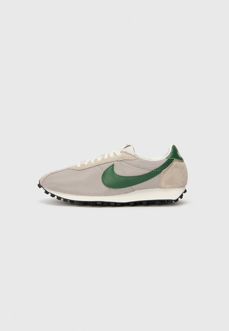 Μπεζ αθλητικά παπούτσια με πράσινες σουέτ λεπτομέρειες, υφασμάτινο επάνω μέρος με υφή, κρεμ κορδόνια και μαύρη λάστιχενη σόλα με καρφιά πρόσφυσης.