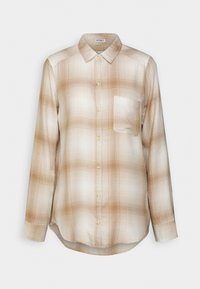 Camicia a maniche lunghe a quadri in beige e crema. Presenta un colletto con bottoni, tasca frontale e un tessuto morbido e testurizzato con una vestibilità comoda.