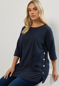 Tunic in maglina a costine blu navy con maniche a tre quarti, caratterizzata da bottoni in argento sul lato e una vestibilità comoda. Tessuto liscio.