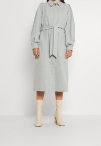 Manteau gris clair, longueur genou, avec une taille ceinturée, un grand col et des manches volumineuses. Associé à des bottes stiletto crème jusqu'au genou.