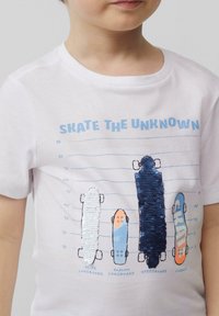 Witte T-shirt met kleurrijke, met pailletten versierde graphics van vier skateboards met verschillende ontwerpen en labels: Slide, Slalom, Speedboard, Classic.
