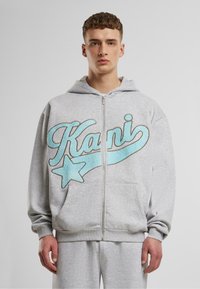 Pelēka ar rāvējslēdzēju kapuce ar lielu zilu un zelta izš�ūtu "Kani" logo un zvaigznes detaļu. Aprīkota ar regulējamu kapuci un priekšējiem kabatām.