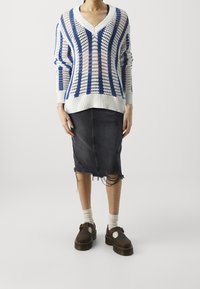 Suéter de punto blanco y azul con escote en V y tejido abierto, combinado con una falda lápiz de mezclilla oscura desgastada y zapatos marrones.