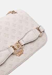 Borsa in pelle color crema con motivo in rilievo del logo, hardware dorato e una tracolla decorativa con dettaglio ad anello e fibbia.