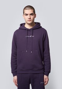 Purple hoodie made of soft fabric, featuring a front pocket, drawstring hood, and a white logo embroidered on the chest.