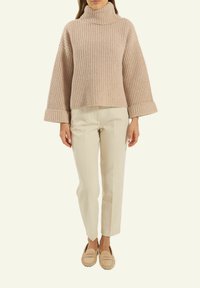 Helles rosa geripptes Oberteil mit hohem Kragen, weiten Ärmeln und aufgerollten Bündchen, kombiniert mit cremefarbener maßgeschneiderter Hose und beigen Mokassins.