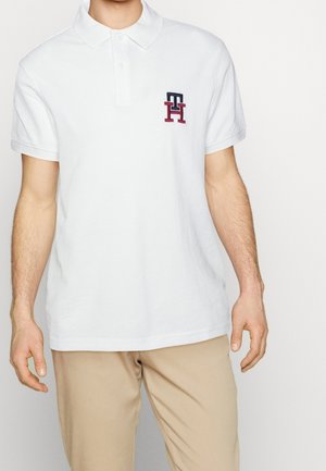 Polo shirt bianco in cotone, con colletto, maniche corte e un piccolo logo ricamato in blu navy e rosso sul petto sinistro.