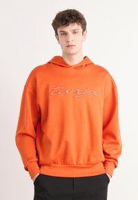 Felpa con cappuccio arancione realizzata in tessuto morbido, caratterizzata da una vestibilità rilassata, polsini a coste e logo ricamato 'targa' dello stesso colore.