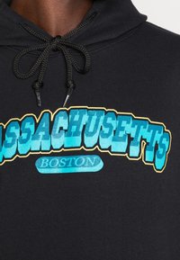 Černá mikina s kapucí s modrým a žlutým grafickým nápisem "MASSACHUSETTS" a "BOSTON", s utahováním na šňůrku a texturovanou látkou.