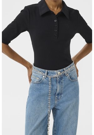 Person wearing black buttoned polo shirt tucked into light blue jeans with a long silver chain belt hanging down the front.