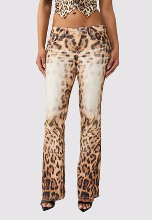 Femme portant un pantalon taille haute à imprimé léopard avec des détails blancs délavés, associé à des talons noirs ouverts à l'avant et un haut assorti à imprimé léopard.