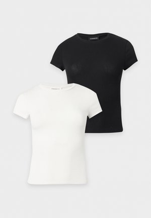 Lachende vrouw met lang donker haar draagt een zwart aangesloten topje met korte mouwen, losse olijfgroene broek met elastische boorden en zwarte sandalen.