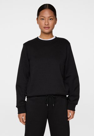 Sort sweatshirt i blødt materiale med rund halsudskæring, ribbestrikkede manchetter og en subtil logo-detail. Parret med matchende sorte bukser.