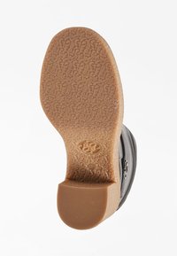 Chaussure noire avec une semelle texturée, présentant une semelle extérieure en caoutchouc marron clair et un léger talon. Dotée d'un bout rond et d'une surface supérieure lisse.