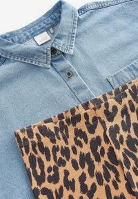 Chemise en denim bleu clair avec un col pointu, des boutons de fermeture et une poche, associée à un pantalon en velours côtelé beige avec un imprimé léopard noir.