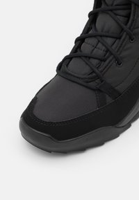 Zapatilla ligera negra con parte superior de tejido texturizado, superposiciones suaves, sistema de cordones prominente y suela acolchada.