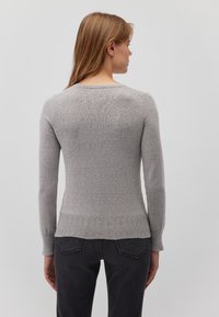Grauer, taillierter Pullover mit langen Ärmeln und geripptem Saum. Glatte Textur und runder Ausschnitt. Getragen mit dunklen Jeans, die ein schlichtes Design zeigen.