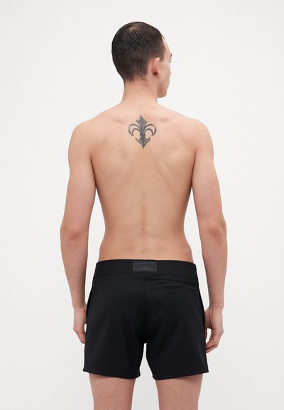 Bañadores negros de tela texturizada, con cinturilla elástica y un bolsillo trasero. Presenta un logo visible en la cinturilla.