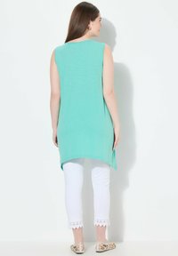 Un top senza maniche di un verde menta con un orlo arrotondato, abbinato a pantaloni bianchi con un bordo in pizzo sulle caviglie, indossato con delle ballerine a fantasia.