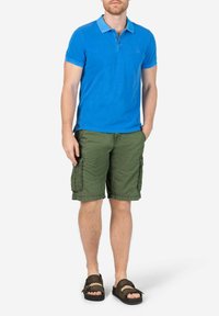 Blaues Baumwoll-Polohemd mit einem kontrastierenden Kragen, kombiniert mit grünen Cargo-Shorts mit Seitentaschen und braunen Sandalen.