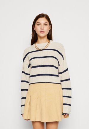 Knit sweater in beige with navy horizontal stripes and a crew neckline, paired with a pleated light yellow corduroy skirt. Gold chain necklace.